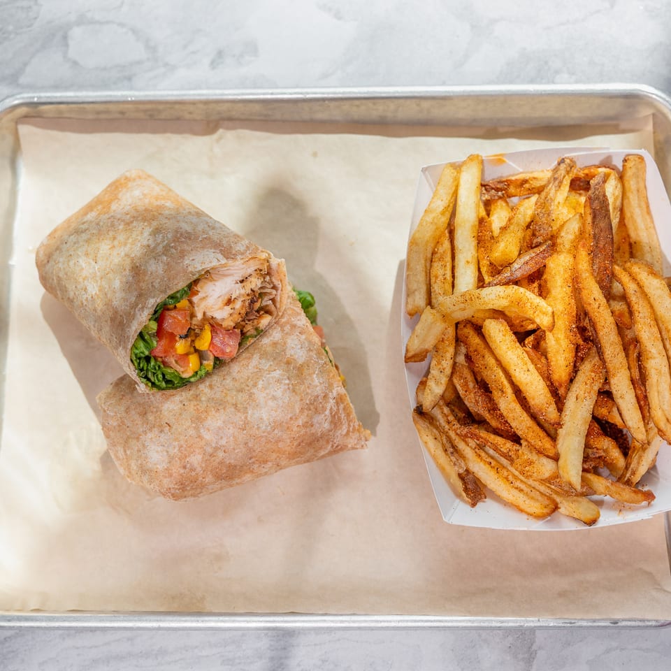 Chicken and vegetable wrap served with seasoned french fries on a parchment-lined metal tray.