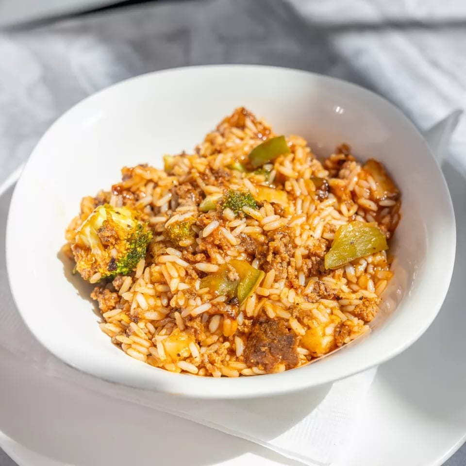 Bowl of tomato-seasoned rice with ground meat, broccoli, peppers, and melted cheese on a white plate.
