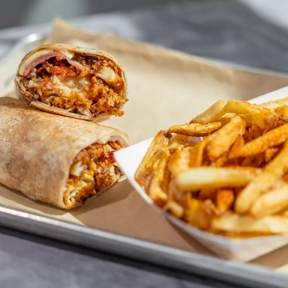 Two stuffed burritos, one sliced open, served with seasoned fries on a paper-lined tray.