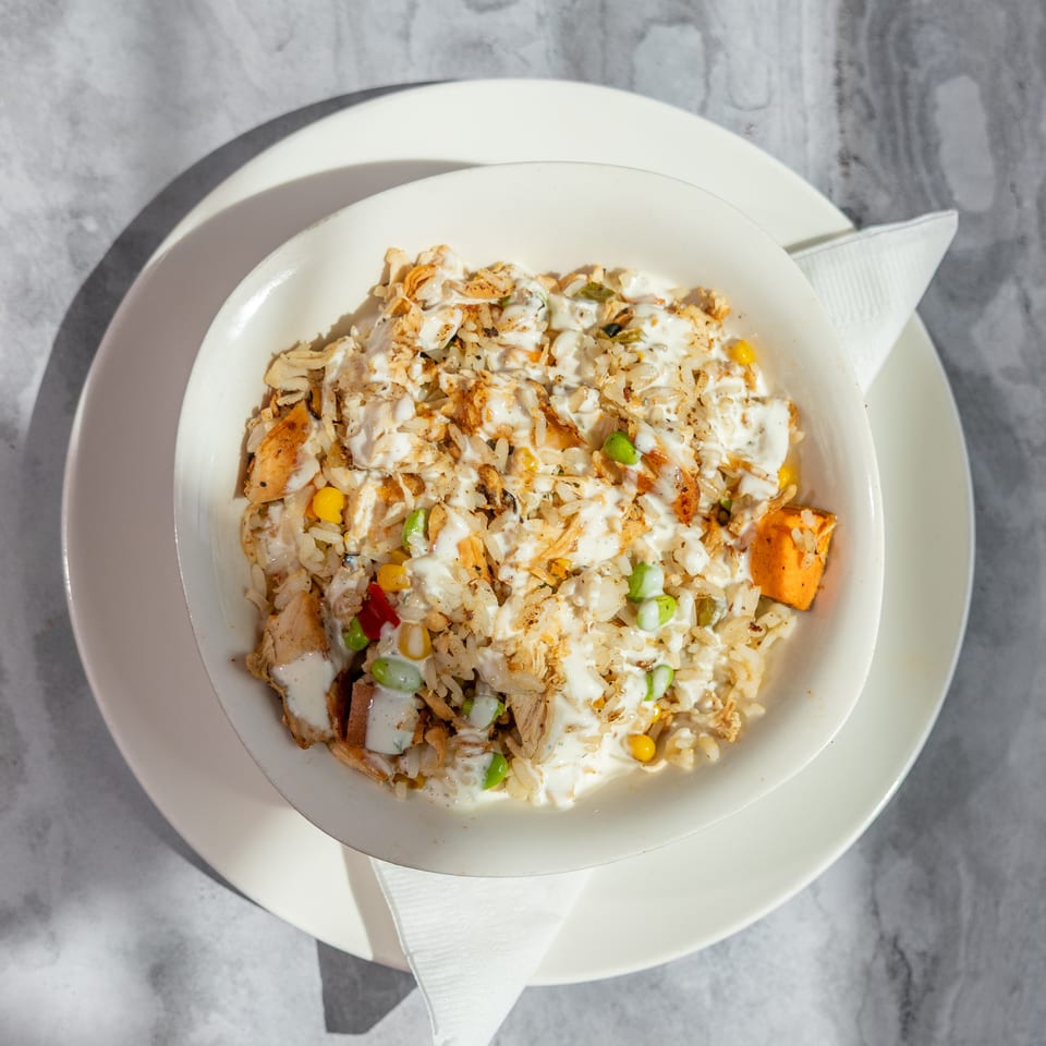 Bowl of seasoned rice with grilled chicken, mixed vegetables, and creamy white sauce on a white plate.