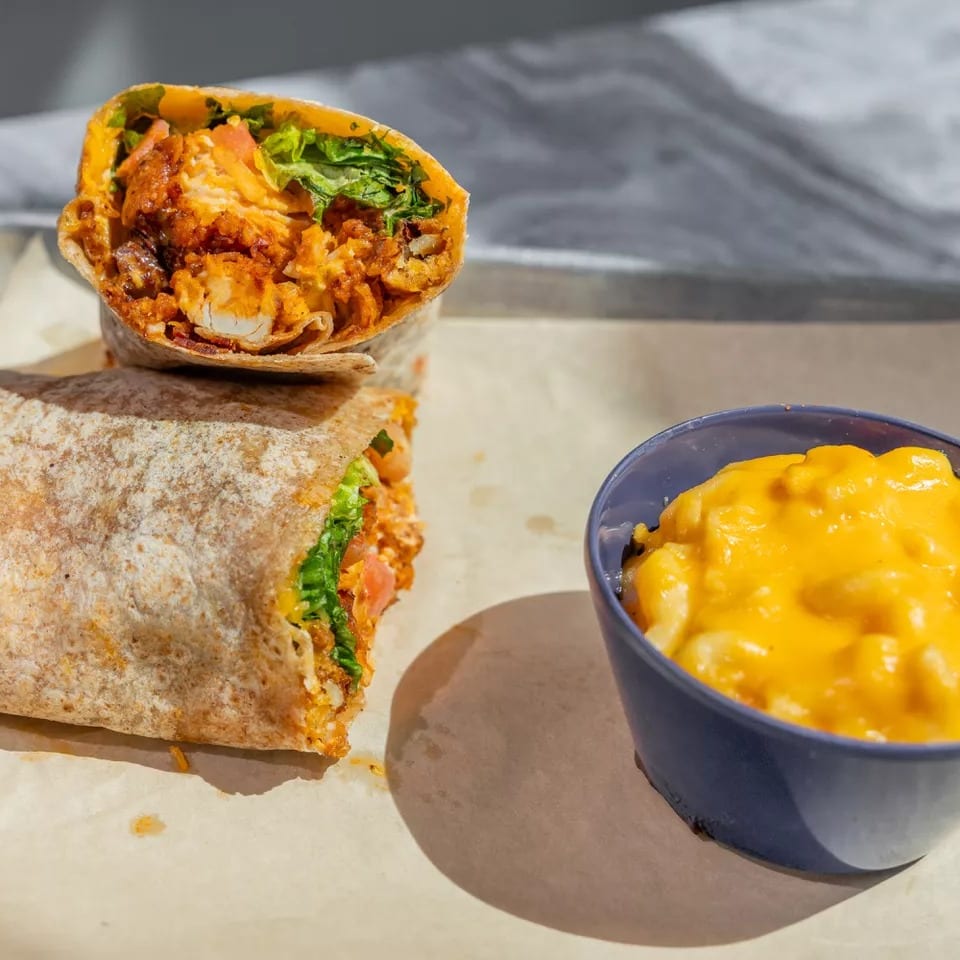 A cut-open chicken burrito with lettuce and tomatoes sits beside a bowl of creamy macaroni and cheese.