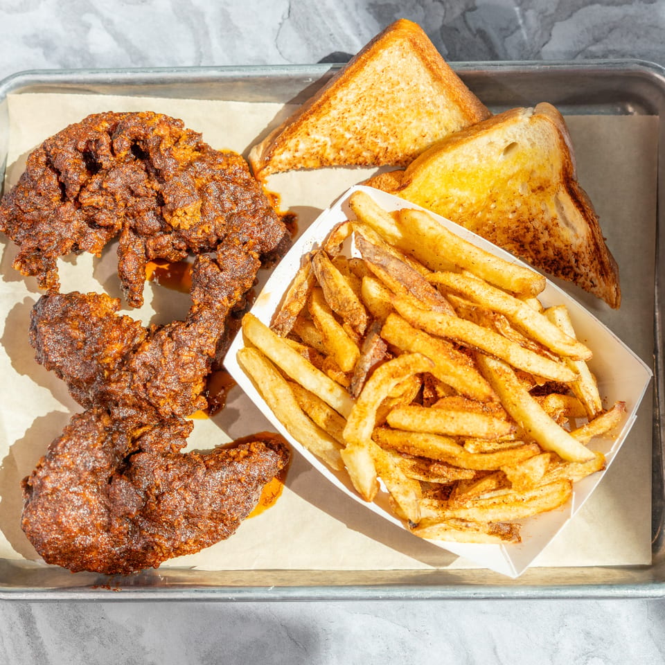 Crispy fried chicken, seasoned French fries, and toasted bread served on a parchment-lined metal tray.