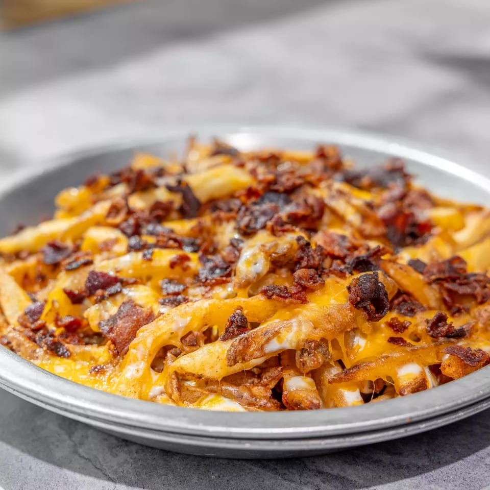 Loaded fries topped with melted cheese and crispy bacon served on a metal plate.